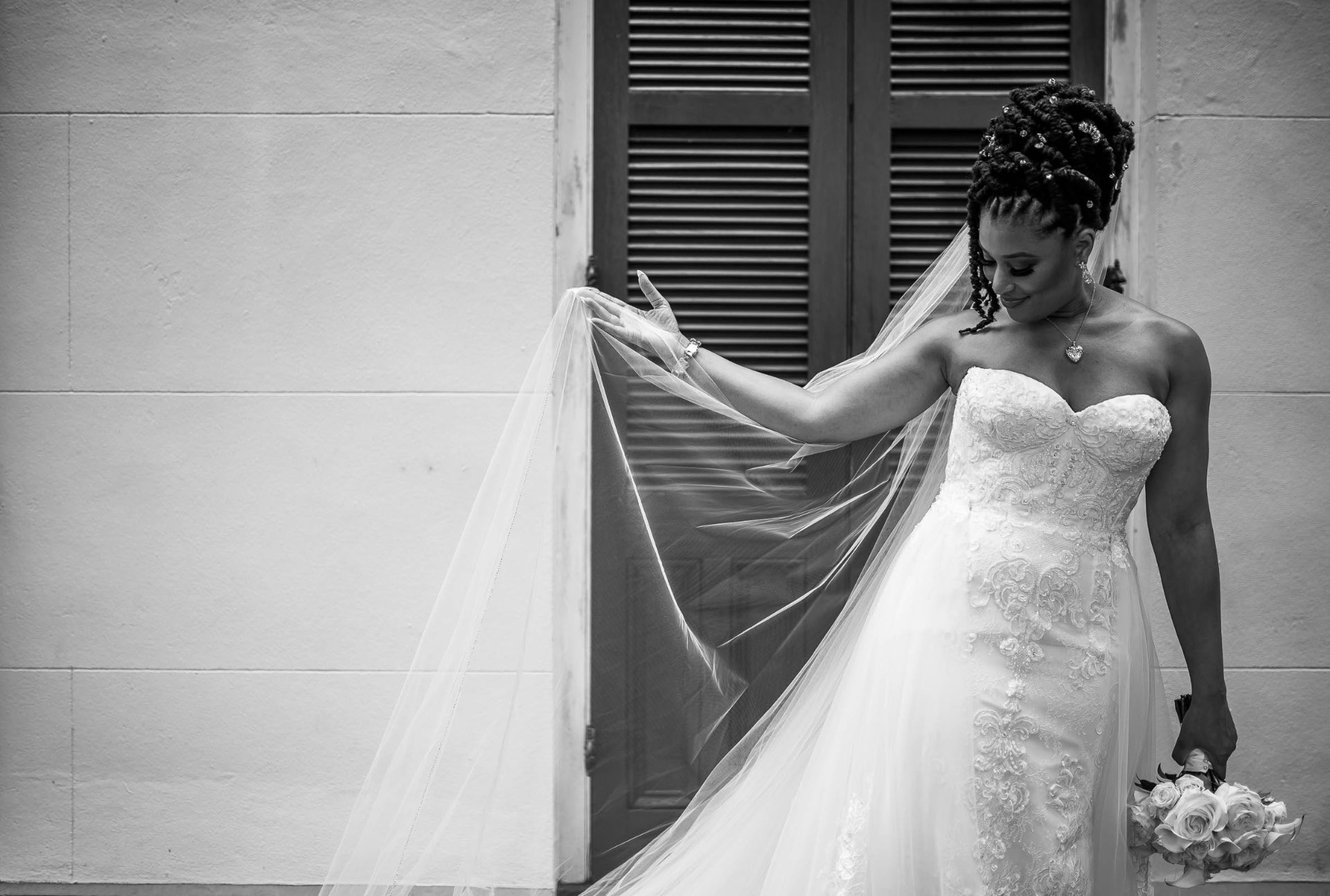 Bride with veil by shutters black and white bouquet