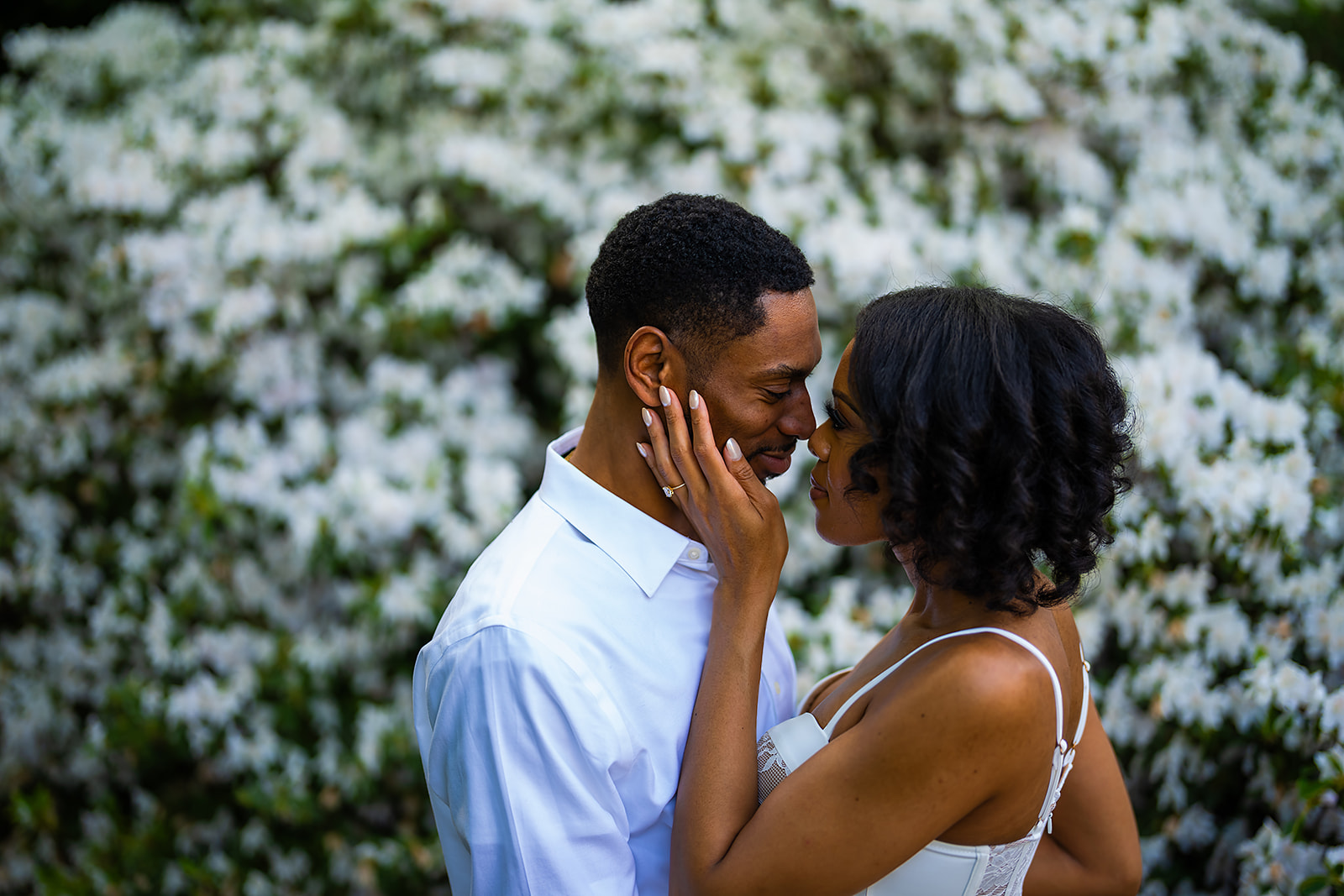 Couple almost kiss in front of white blossoms garden intimate