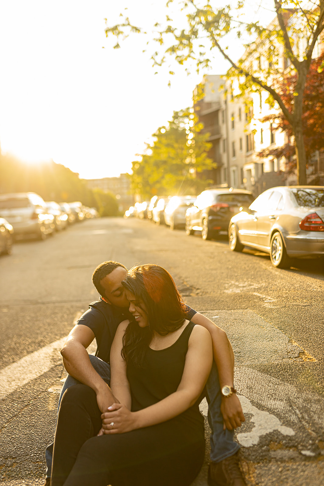 Couple cuddle on street curb at golden hour
