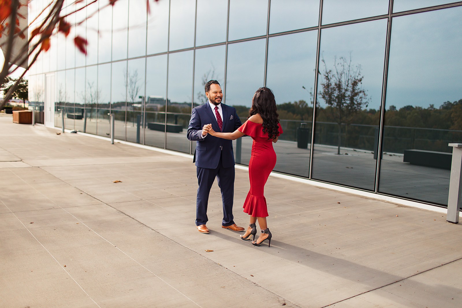 Couple dancing at glass building in red dress and navy suit autumn