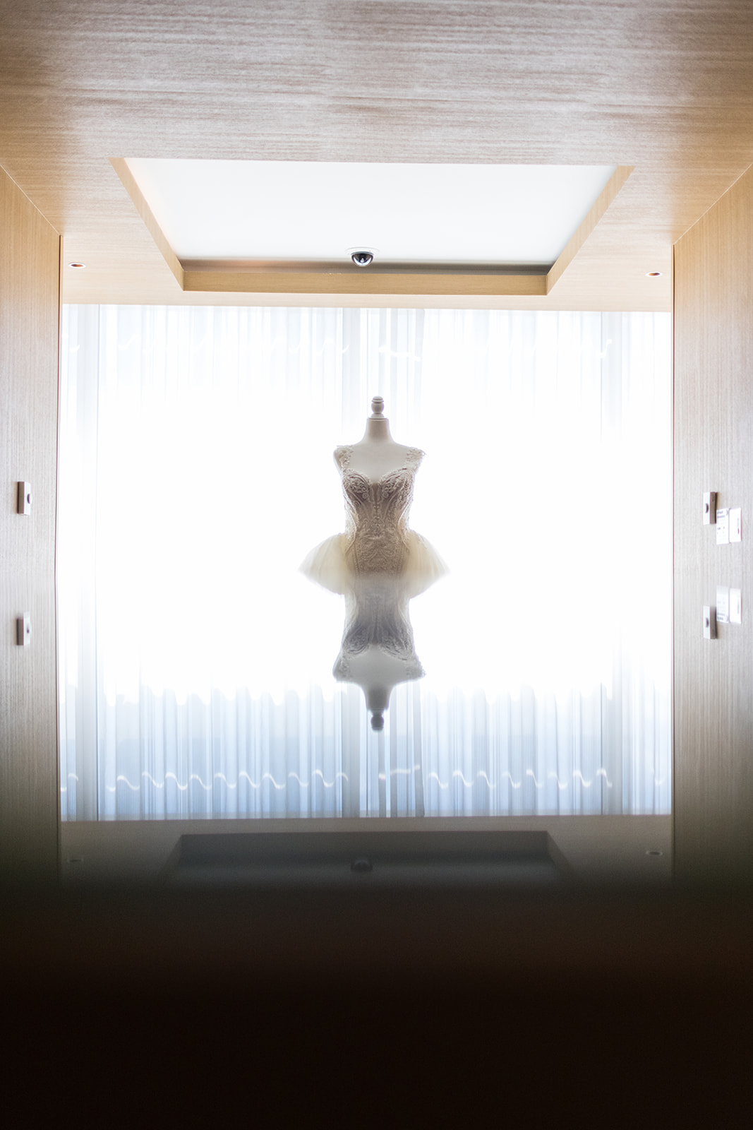 Bridal gown on mannequin silhouetted against hotel window with reflection