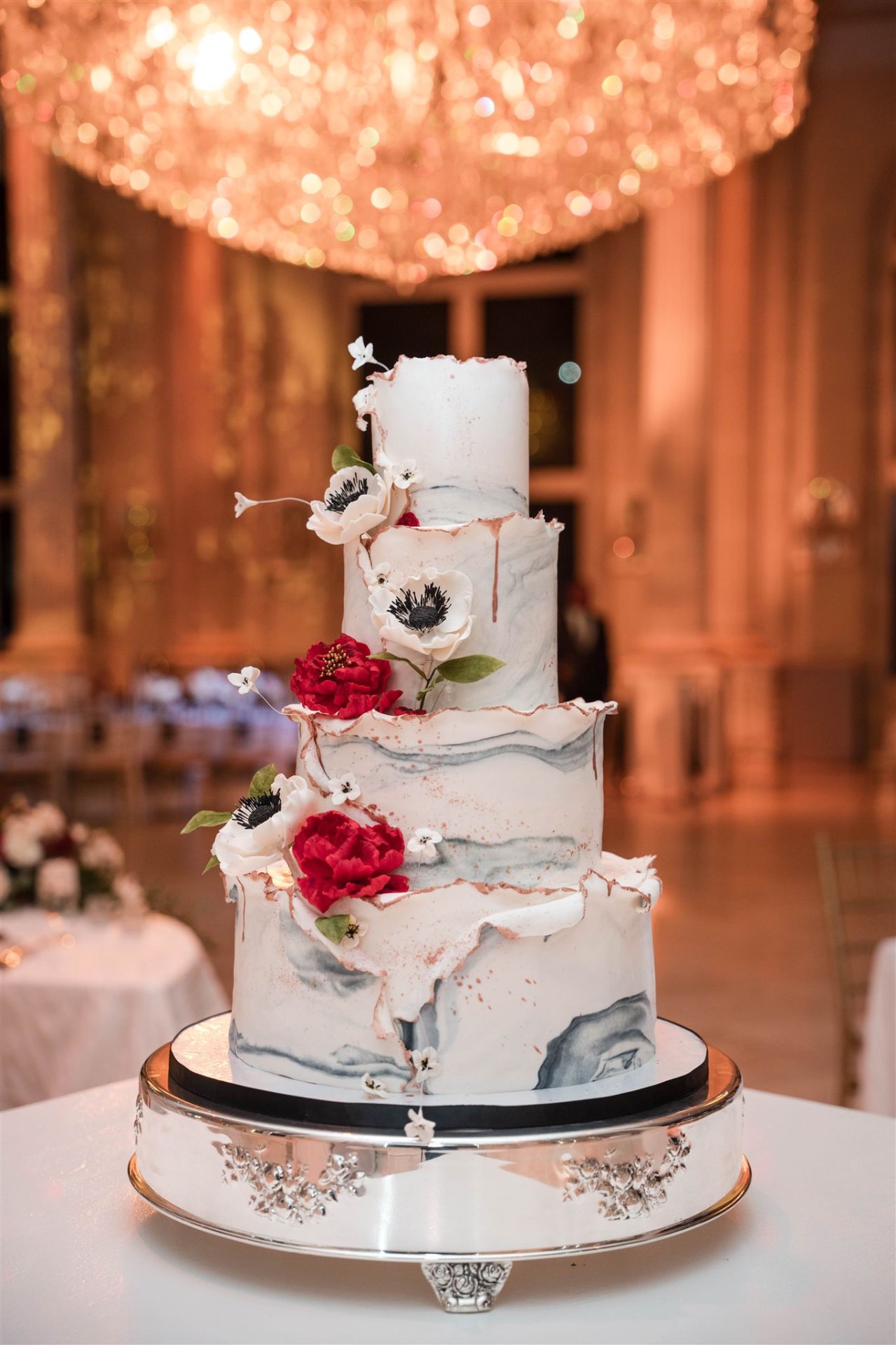 Four-tier marble wedding cake with anemones red peonies under crystal chandelier
