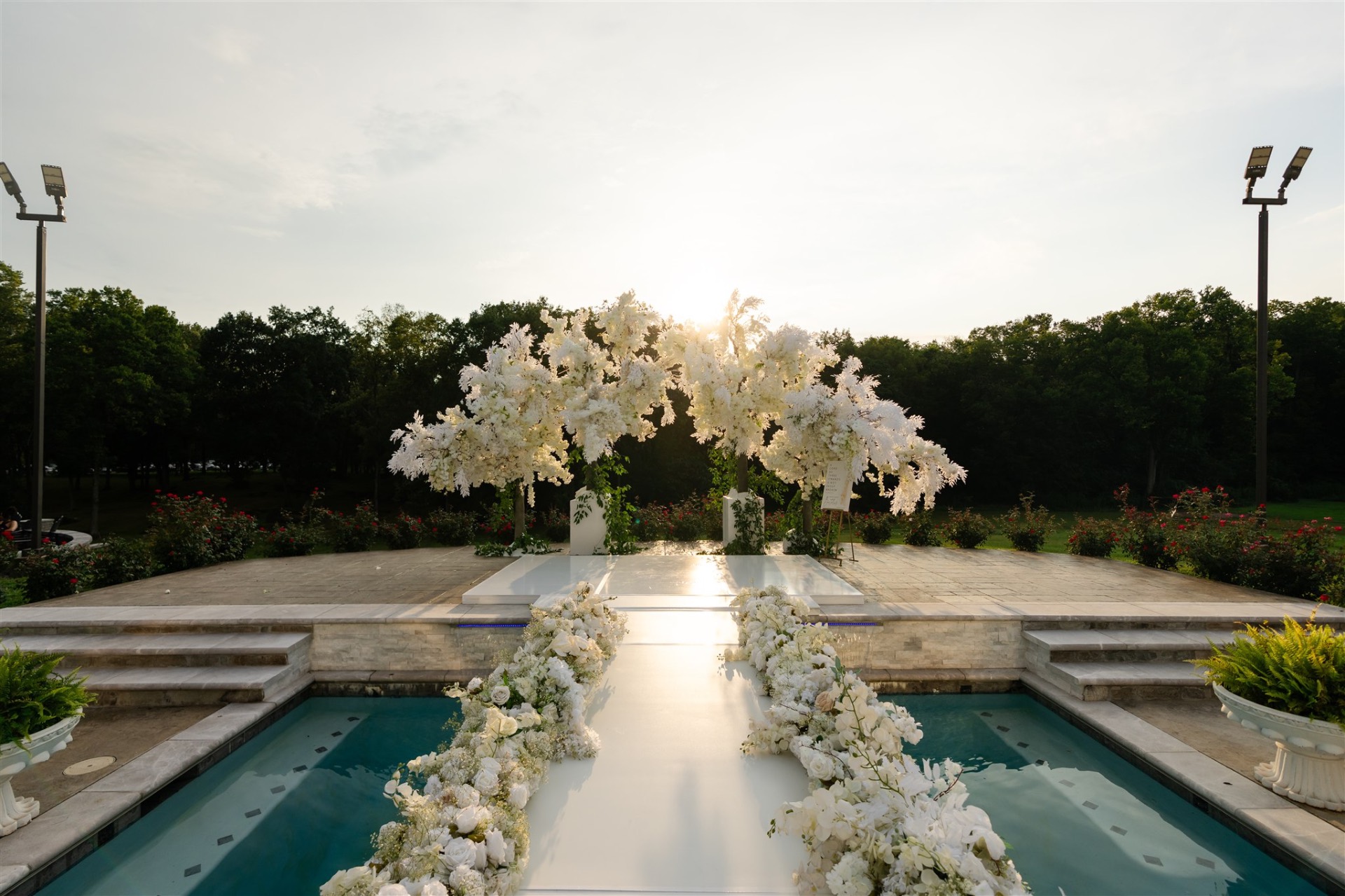 Outdoor ceremony arch white florals poolside aisle at sunset