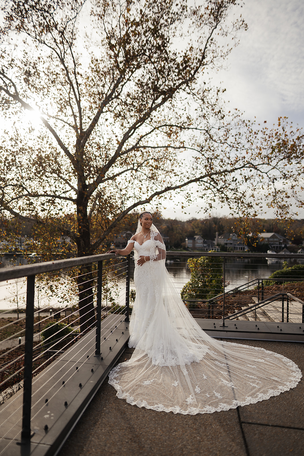 Bride on autumn lakeside balcony with cathedral veil and train