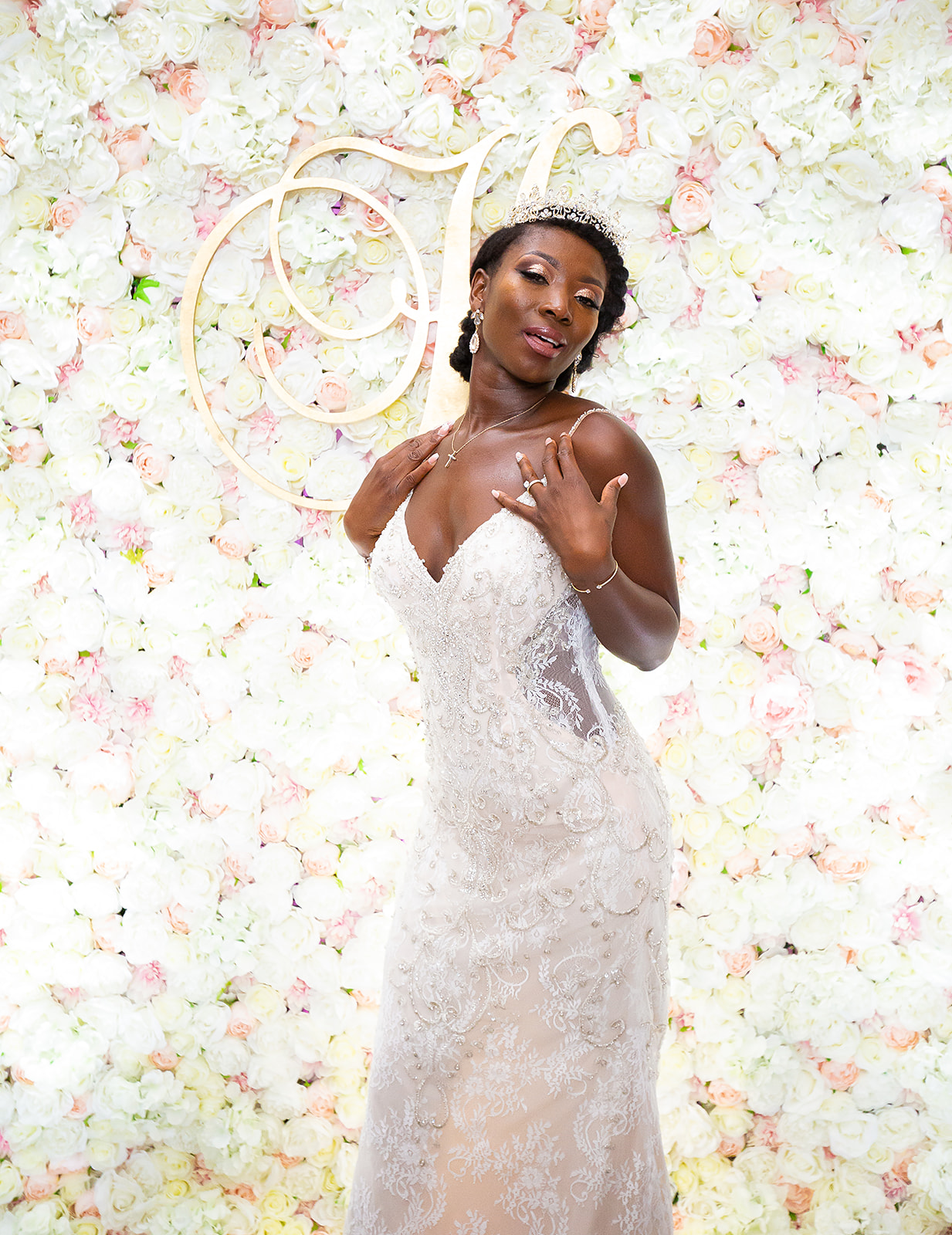 Bride posing against flower wall with tiara and lace gown portrait