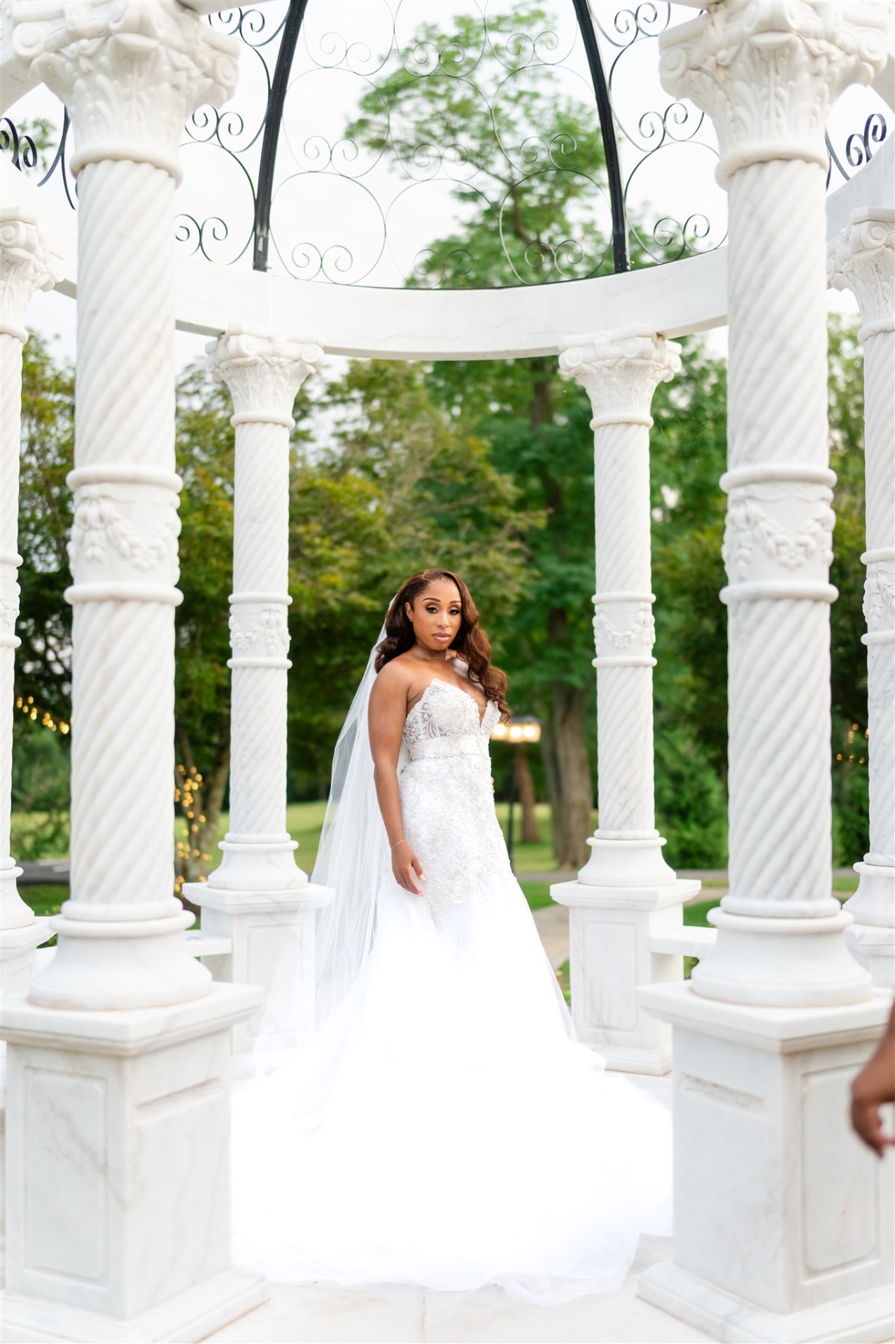 Bride in lace gown standing in white marble gazebo with veil