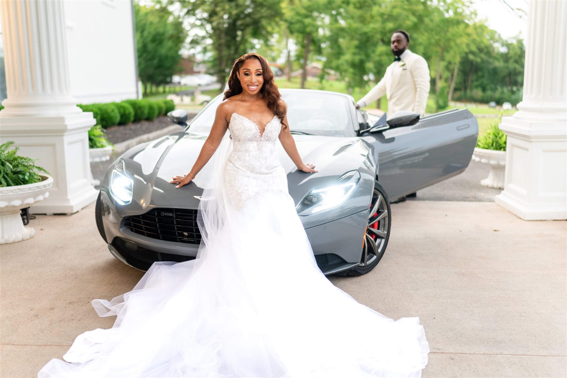 Bride and groom with luxury sports car at mansion columns