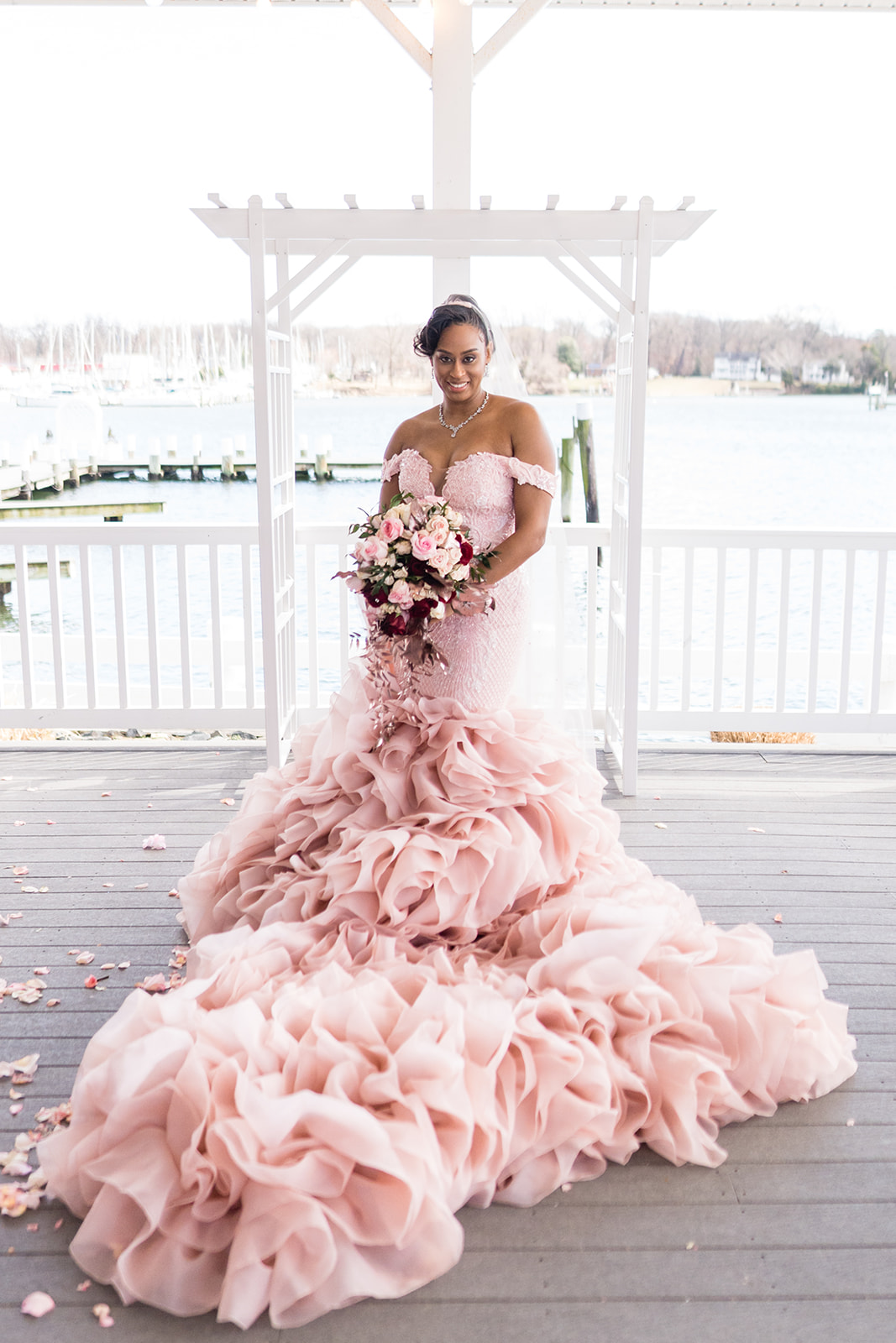 Bride in pink ruffled mermaid gown with bouquet at waterfront