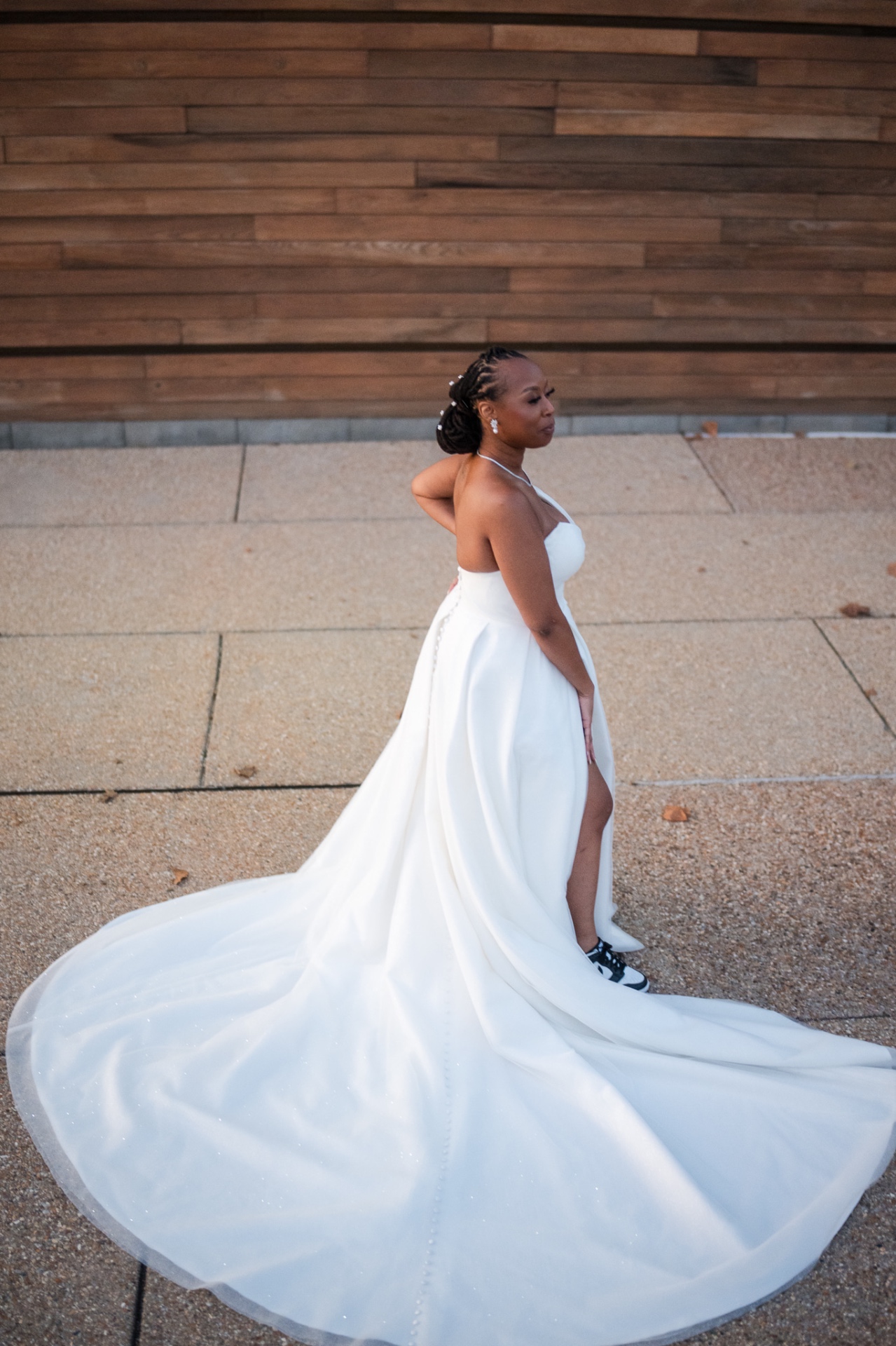 Bride in satin gown with sneakers flowing train wood wall portrait