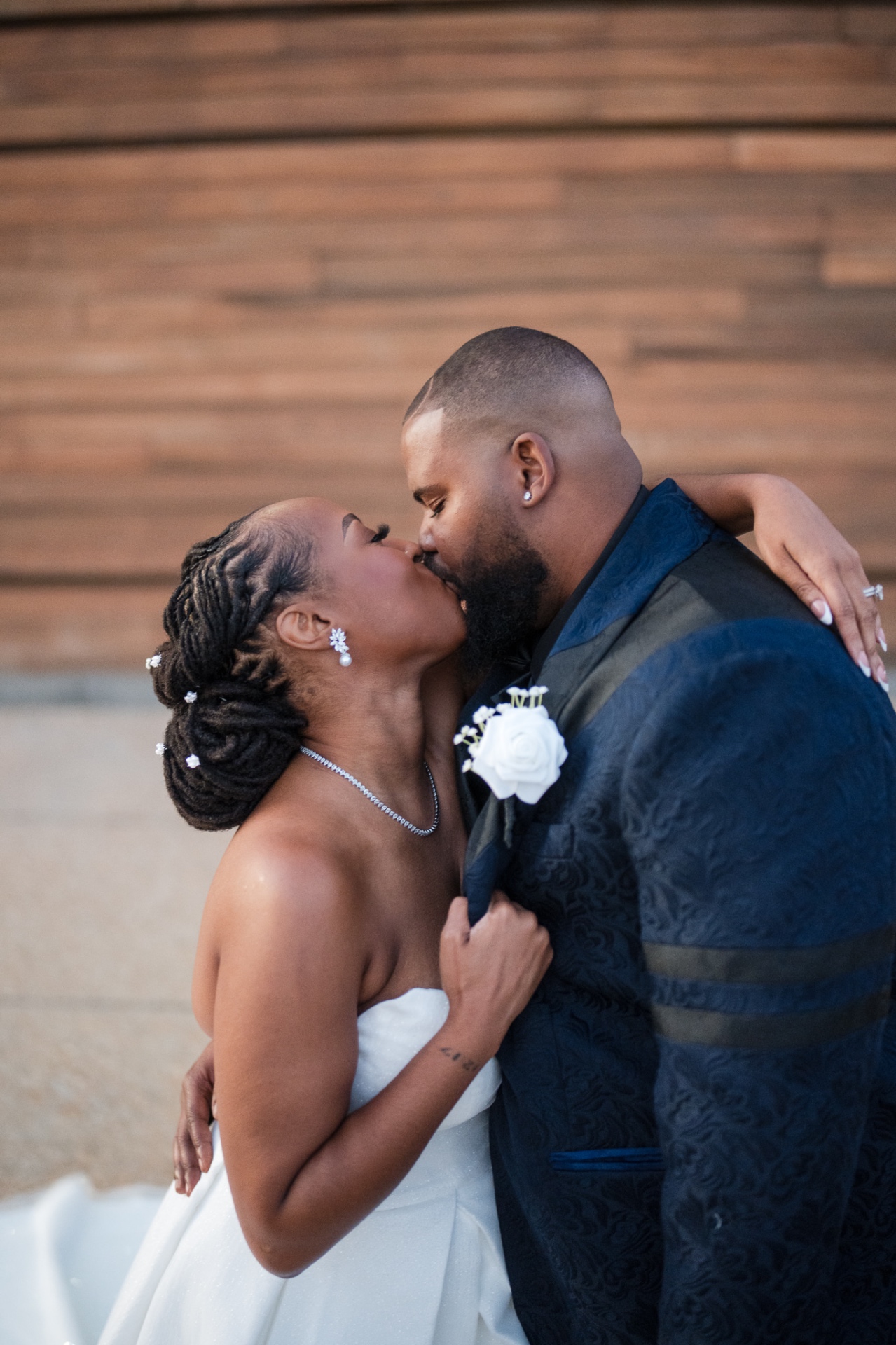 Couple kiss bride with locs updo groom brocade tuxedo wood backdrop