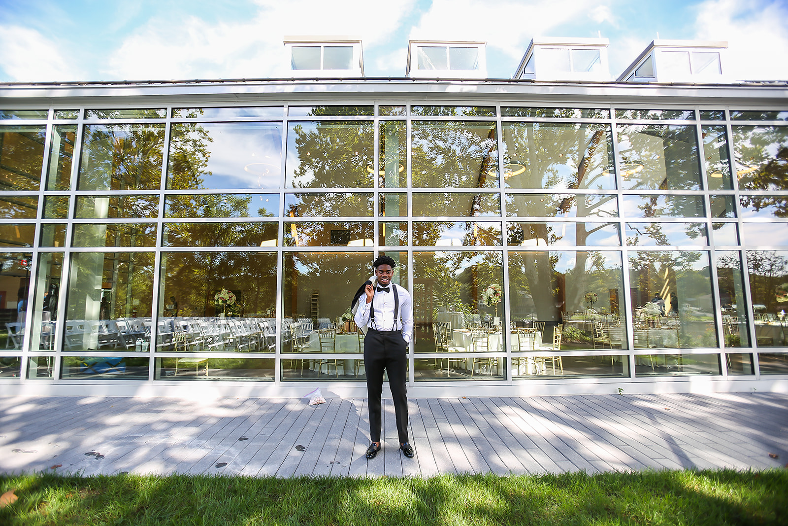 Groom in suspenders and bowtie at glass venue with reflection portrait