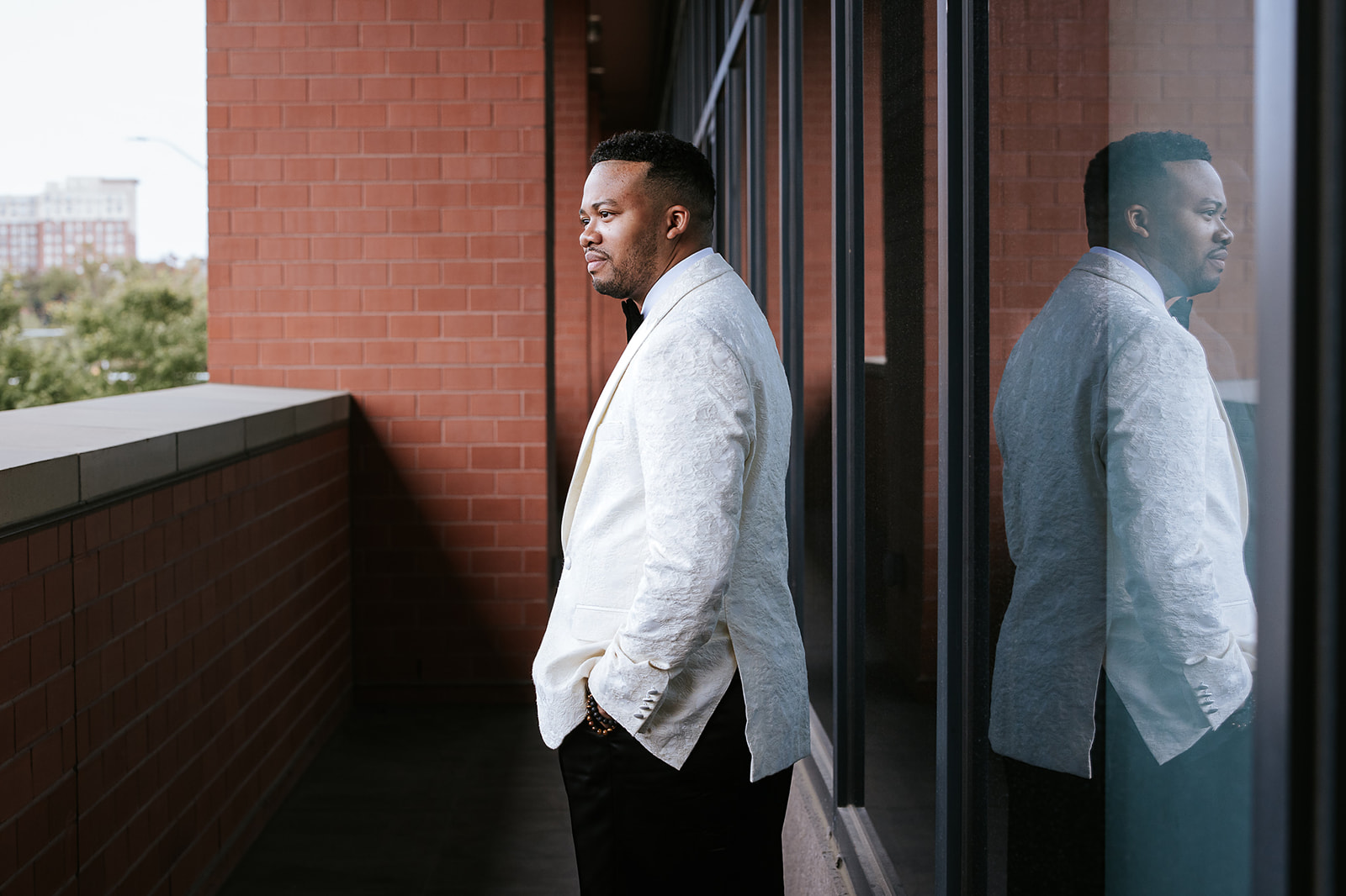 Groom in white jacket on brick balcony with glass reflection