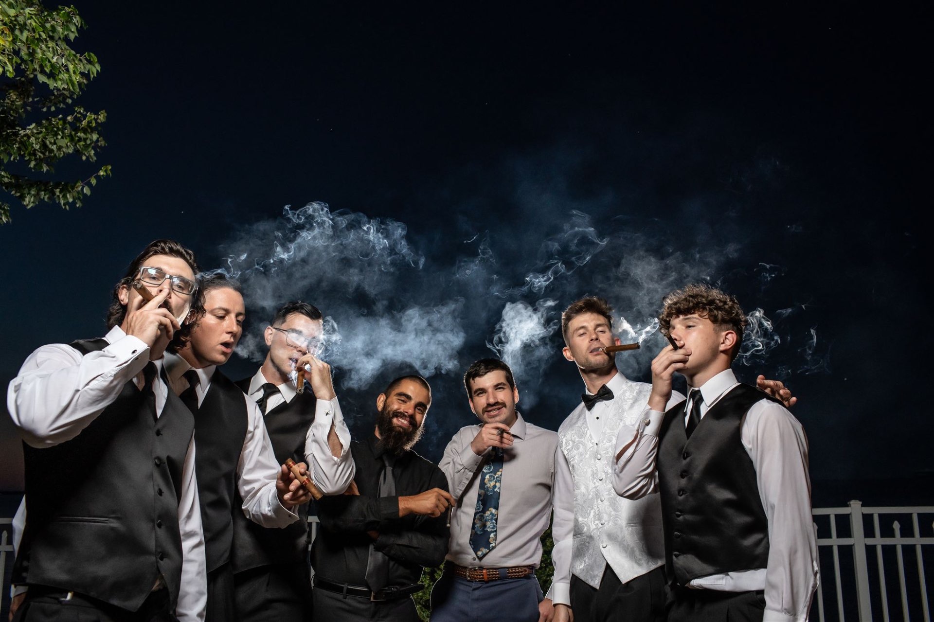 Groomsmen smoking cigars at night celebration portrait