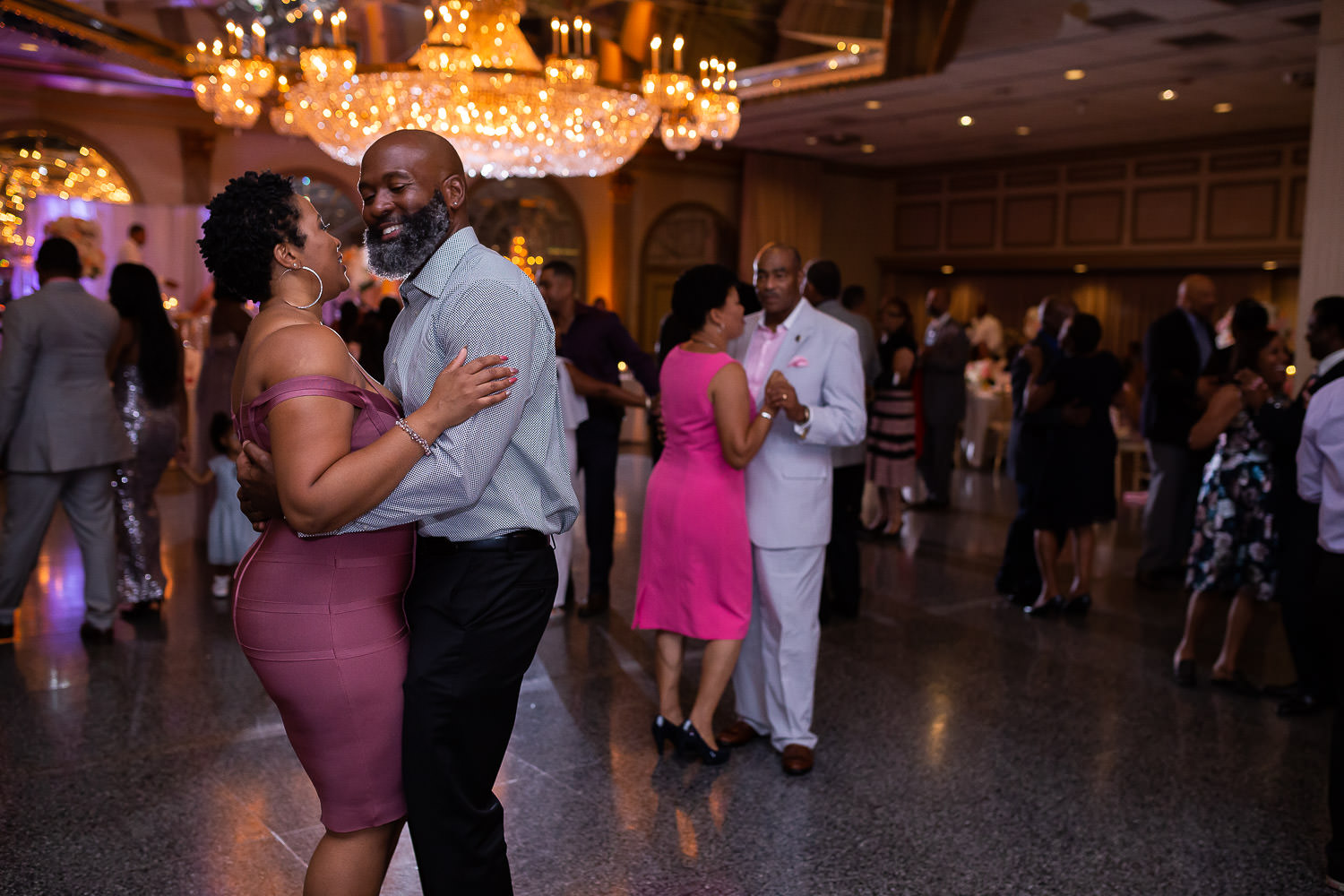 Wedding guests dancing in ballroom under chandelier candid