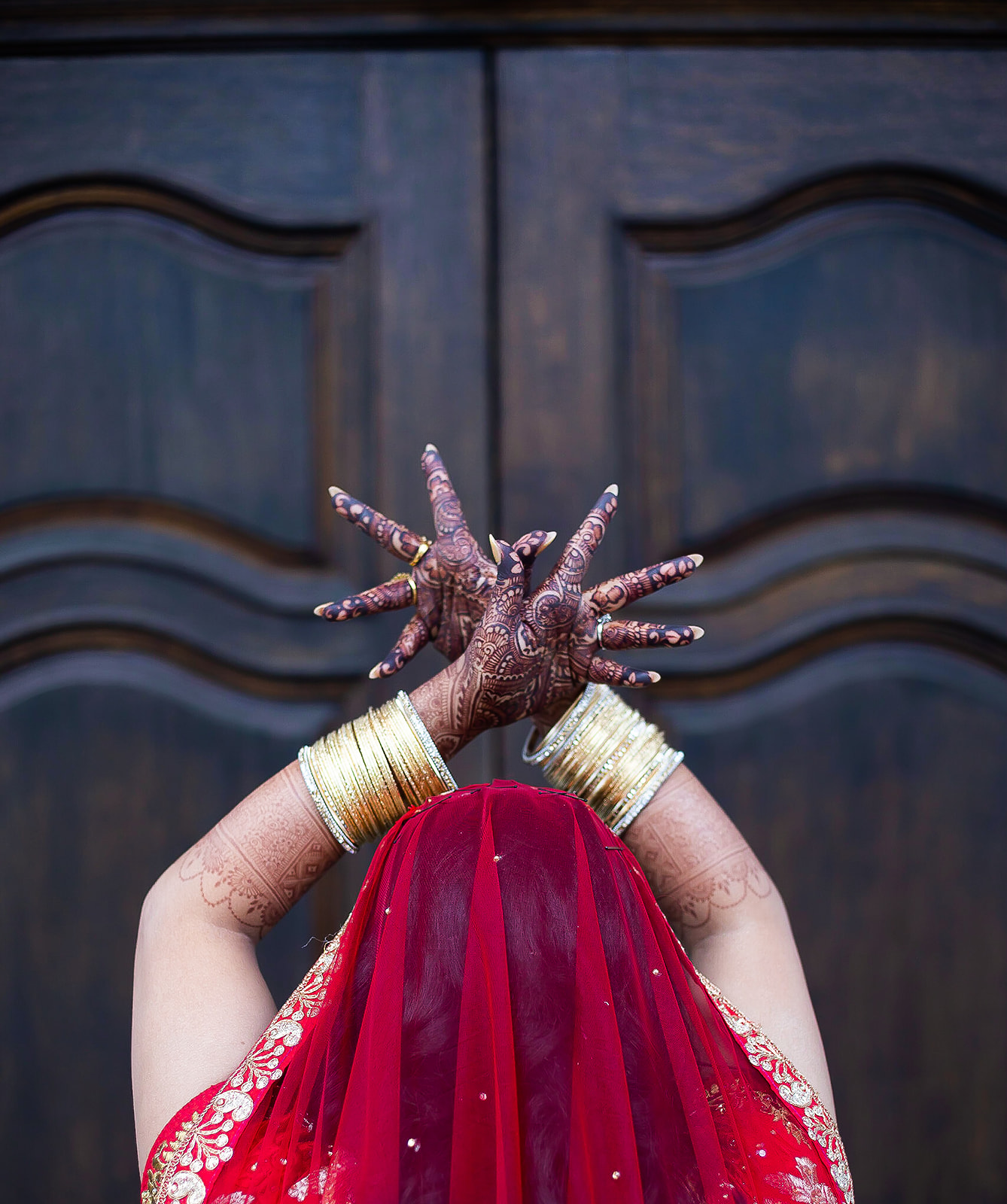 South Asian bride henna hands raised red veil wooden door